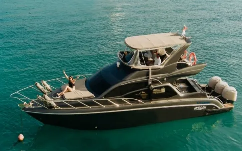A dark grey motor yacht anchored in clear green water