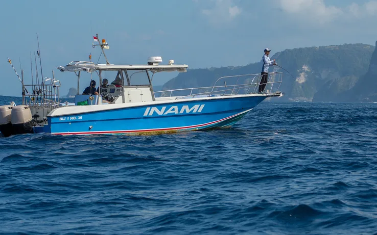 A blue and white sport fishing boat off the cliffs of Nusa Penida